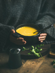 Woman in dark grey woolen winter sweater eating sweet corn and shrimp chowder soup from black bowl....