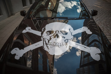 Ein Totenkopf Symbol auf der Motorhaube eines Autos mit Reflektionen von Wolken und Häusern
