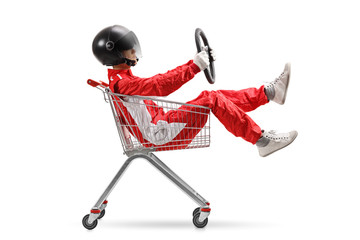 Guy in a racing suit with helmet holding a steering wheel and sitting inside a shopping cart