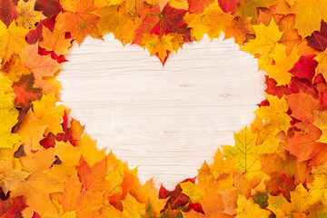 Heart shape bright maple autumn leaves frame on wooden background