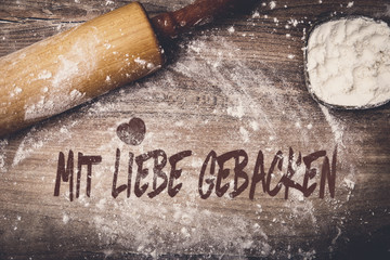 Teigrolle und Mehl auf Tisch, Text mit Liebe gebacken auf Holz