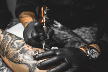 The tattoo artist creates a picture on the body of a man. close-up of tattoo machines and hands