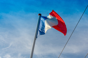 french flag waving in front of a blue, slightly cloudy sky