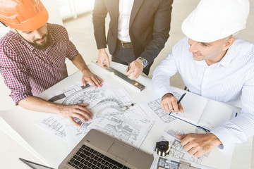 male engineers, architects working at the desk in helmets. Drawings, laptop, roulette on the...