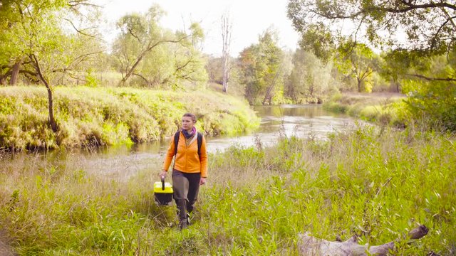 Woman scientist ecologist goes from the river, puts the tool box on the ground gets a laptop and turns it on