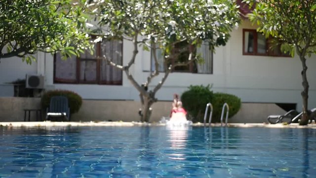 A man stands by the pool in red shert and jumps his head into the blue water. HD, 1920x1080, slow motion