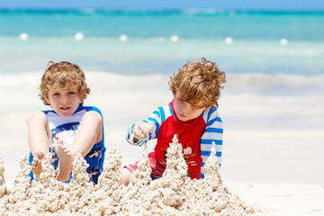 Two kid boys building sand castle on tropical beach of Maldives