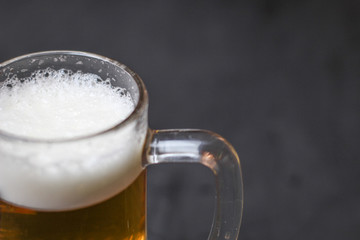 Light beer with a white fluffy foam on a dark background