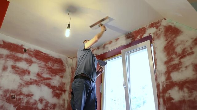 construction worker plastering ceiling with taping knife