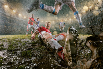 Soccer players performs an action play on a professional night rain stadium. Dirty players in rain...