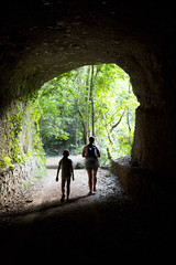 Backlight of mother and daughter coming out of a cave in a forest
