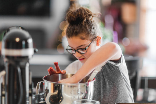 Girl putting ingredients into mixing bowl for christmas cookies at kitchen counter
