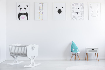 Posters on white wall in minimal kid's room interior with cradle and blue pillow on stool. Real photo © Photographee.eu