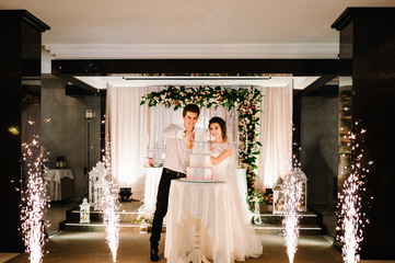 Bride and a groom is cutting their rustic wedding cake on wedding banquet. Hands cut the cake and...