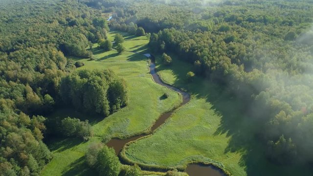Aerial view of beautiful curvy river flowing between forest and green grassland