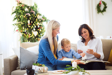 A small boy with mother and grandmother looking at photos at home at Christmas time.