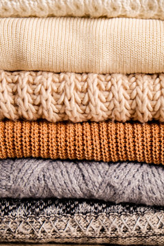 Bunch of knitted warm pastel color sweaters with different knitting patterns folded in stack, clearly visible texture. Stylish fall / winter season knitwear clothing. Close up, copy space for text.