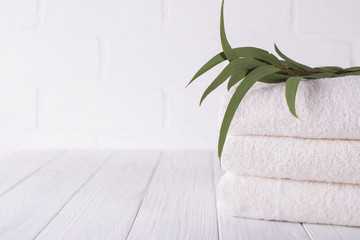 Spa composition on wooden table. Stack of three white fluffy bath towels with eucalyptus branch....