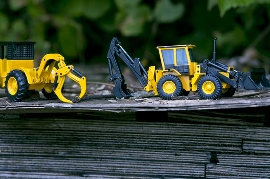 There are two excavator toy cars on wooden boards stacked in the open woods.