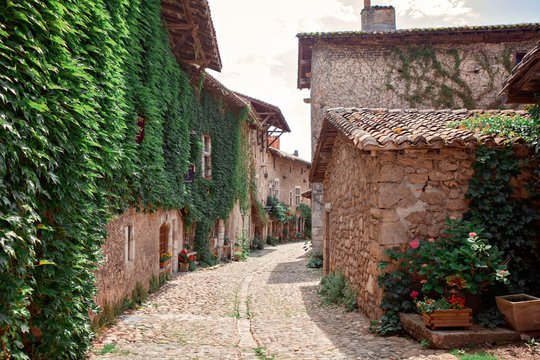 Ancient medieval walled town Perouges. Commune in the Ain department in eastern France. Old stone houses with grapes on the wall. Beautiful street with red flowers in the small town