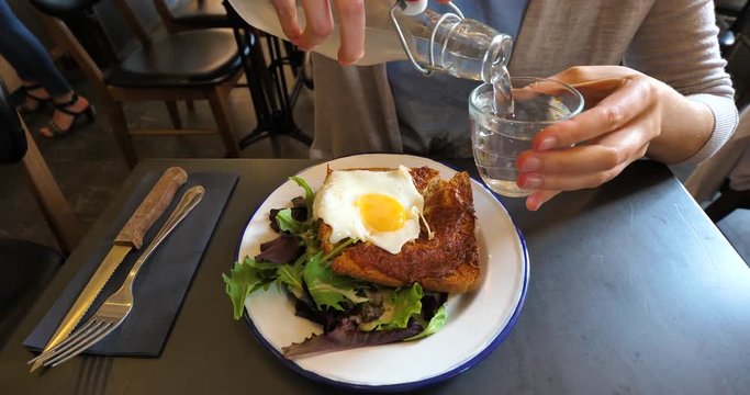 Woman eating delicious croque monsieur - a baked fried boiled ham and cheese sandwich croque madame variant topped with a fried egg