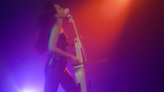 Cellist with electronic cello performs on stage.