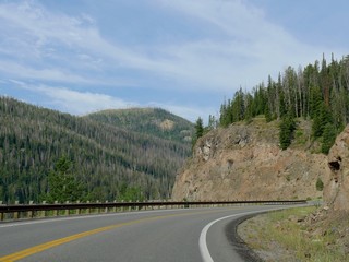 Paved roads winding around rocky cliffs with green mountains at Yellowstone National Park.    