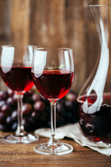 Red wine, decanter, two glasses and dark grapes on a wooden background