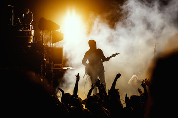 Silhouette of guitar player, guitarist perform on concert stage. Dark background, smoke, concert spotlights.