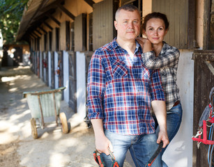 Positive family couple with belly-band standing  at stable outdoor