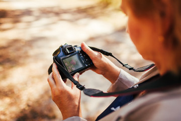 Middle-aged woman checking images on camera in autumn forest. Senior woman walking and enjoying hobby