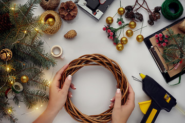 Female hands decorate the Christmas wreath with spruce branches with a red berry and forest cones....
