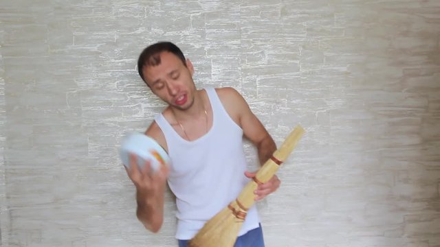 Funny guy with a plate on his head and a broom fooling around and dancing