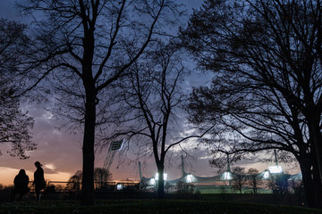 Beleuchtetes Olympiastadion mit Bäumen vor Abendhimmel, München