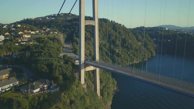 Medium shot of suspension bridge with pillar and landscape. Weather is sunny and there are cars crossing the bridge.