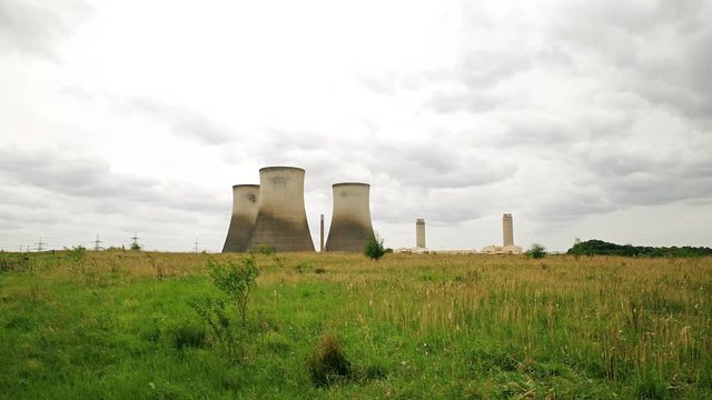 Power station cooling towers seen across green field with rain clouds overhead