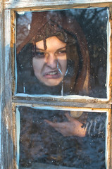young witch is writhing monstrous, full of fierce anger repulsive grimace looks out of the window of his hut clearly showing disgust and disgust to the world
