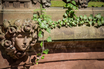 Frauenkopf in einer Steinmauer mit Efeu bewachsen