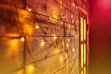 Blur Christmas lights on wooden planks and door. Bright glowing garland. New Year lights background. Yellow red toning