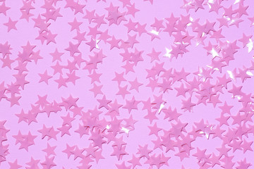 Fototapeta premium Pink sequins on a purple pastel background with confetti as asterisks.