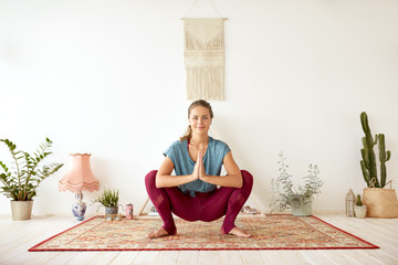 fitness, people and healthy lifestyle concept - young woman doing garland pose at yoga studio
