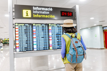 Young asian woman with backpack in international airport looking at the flight information timetables board