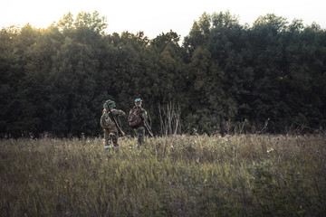 Hunting hunters in  rural field nearby forest at sunset during hunting season