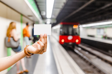 Hand holding blank metro subway ticket at the background of arriving train