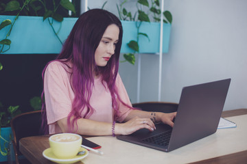Young woman with pink hair with laptop computer sitting in cafe,