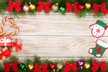 Fototapeta na wymiar Christmas frame made of fir branches decorated with balls, bows, candy canes and boxes on a light wooden background