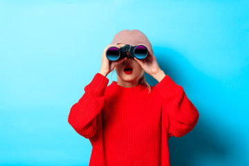 Portrait of a young girl in red sweater with binocular on blue background
