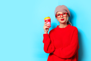 Portrait of a young girl in red sweater with cup of coffee on blue background