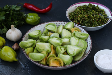 The process of making salad of green tomatoes with pepper, garlic, dill and parsley.