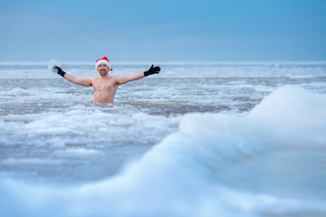 Winter bather in a Santa's hat stays in a frozen sea